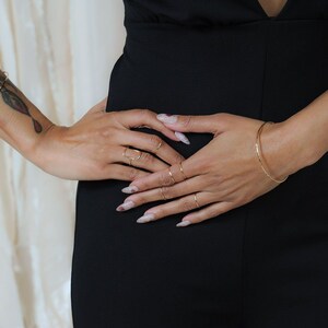 A close-up of a person's hands wearing rings and bracelets, with a black dress visible underneath.