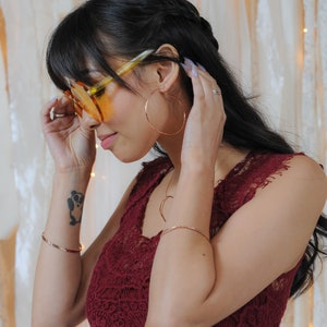 Image shows model wearing a few of our ultra thin 14 karat rose gold filled bangles. Each bangle bracelet is handcrafted from 14 karat Rose Gold Filled. Adding rose gold bangles to any ensemble or stacking bracelet set offers a treat for the senses.