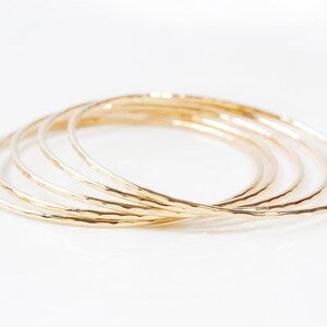 Image shows close up of the exquisite texture of our 14 karat yellow gold filled bangles. Showing five stunning bangles, each bracelet is hand hammered which gives them their special sparkle. Wear individually or stack them up to create a unique set.