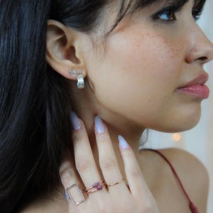 A close-up of a woman's face, with her hand adorned with multiple rings and earrings.