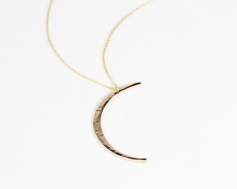 Close up shows the delicate and intentional texture of the moon in 14 karat yellow gold filled. Meant to mimic the look of the moon, the Mystic Moon Necklace elevates celestial jewelry and beams with handcrafted quality.