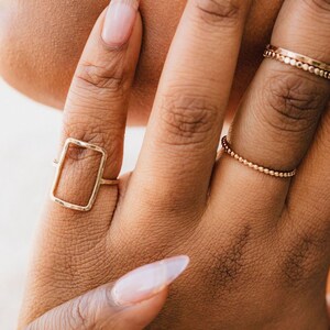 A close-up of a person's hand wearing multiple rings, including a rectangular ring and a ring with small beads.