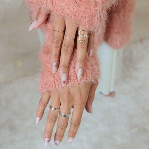 A close-up of a person's hands wearing multiple rings and a pink fuzzy sweater.