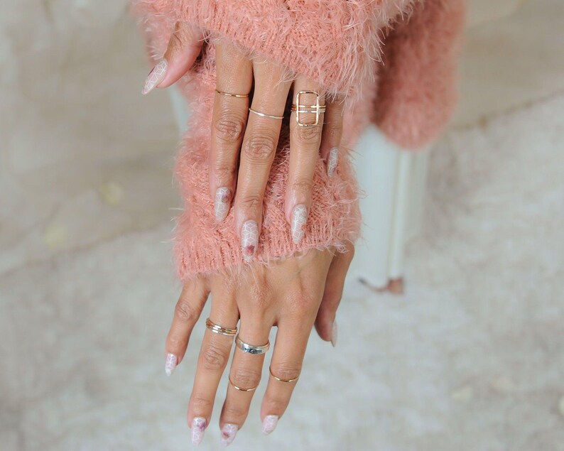 A close-up of a person's hands wearing multiple rings and a pink fuzzy sweater.