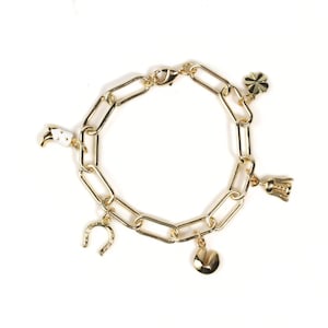 May include: Gold-toned charm bracelet featuring a chain link design. The bracelet includes charms such as a horseshoe, a four-leaf clover, a tooth, a bell, and a heart. The bracelet is displayed on a white background.
