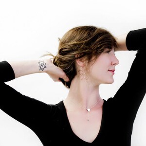 May include: A woman with brown hair wearing a black long-sleeved shirt and silver jewelry. She has a geometric tattoo on her wrist.
