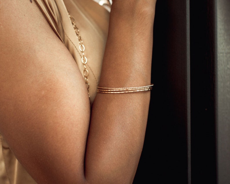 Image shows model wearing a few of our thin hand hammered stacking gold bangles. Each fine metal bangle bracelet is handcrafted from 14 karat Yellow Gold Filled.  This exquisite material is nickel free and perfect for sensitive skin.