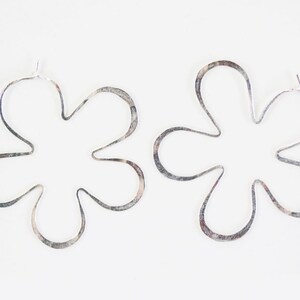May include: A pair of silver flower-shaped hoop earrings. The earrings are made of thin metal and have a delicate, feminine look.