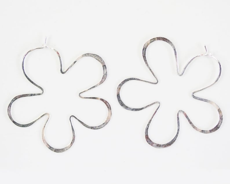 May include: A pair of silver flower-shaped hoop earrings. The earrings are made of thin metal and have a delicate, feminine look.
