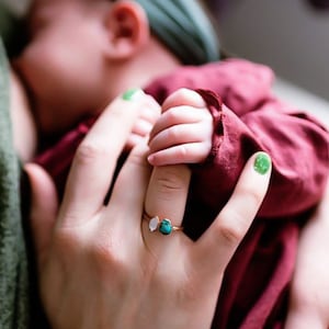 Mother nursing baby wearing our 2 stone raw birthstone ring in copper. Baby holding finger of mother. Birthstone ring in Herkimer diamond and turquoise.