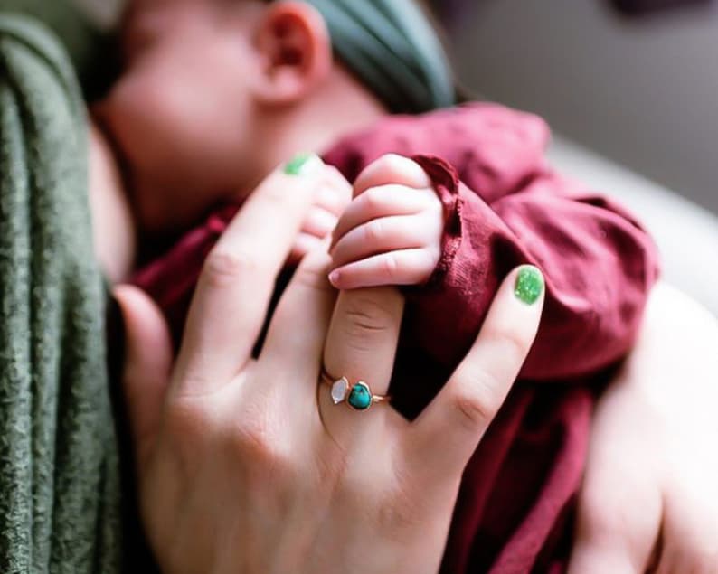 Mother nursing baby wearing our 2 stone raw birthstone ring in copper. Baby holding finger of mother. Birthstone ring in Herkimer diamond and turquoise.