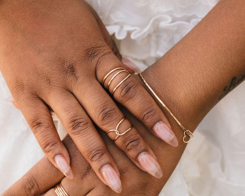 A close-up image of two hands wearing rings and bracelets.