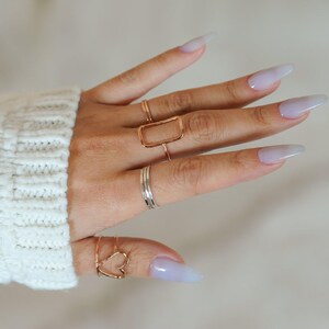 A close-up of a person's hand wearing multiple rings on their fingers, including a ring with a heart design.
