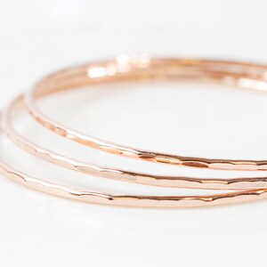 Image shows close up of our ultra thin 14 karat rose gold bangles. Hand hammered for a light texture, each bracelet is high quality and made to stand the test of time.  At a width of 1/16 inch, each stacking bangle will glint and glisten in the sun.
