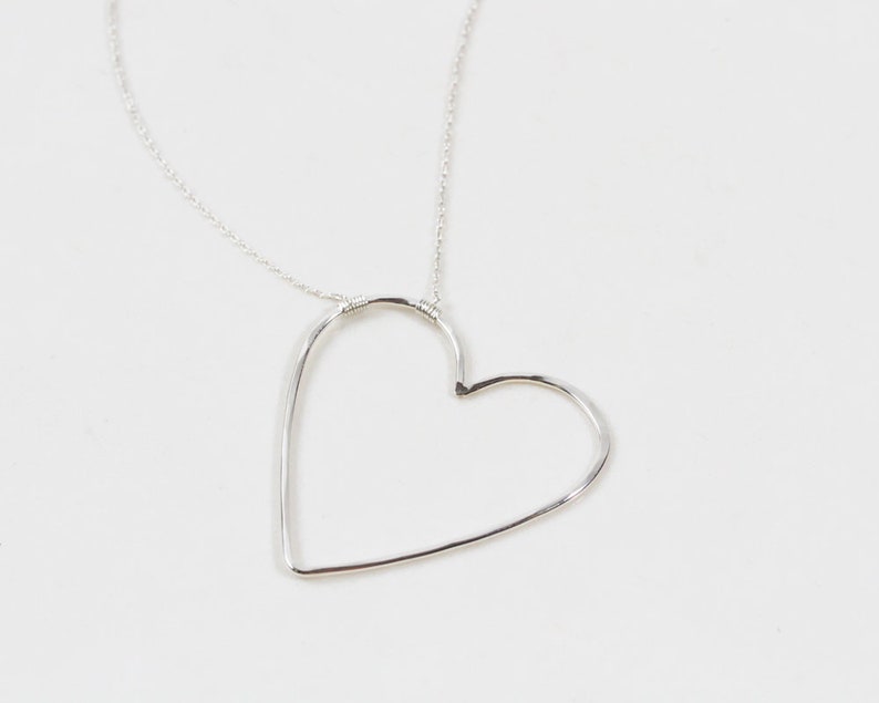 Close up shows our sweet heart necklace in .925 sterling silver. All handcrafted in house by our team of local artisans, each piece is made to order, just for you. Each heart receives a delicate hand hammer texture to cast off shine while being worn.