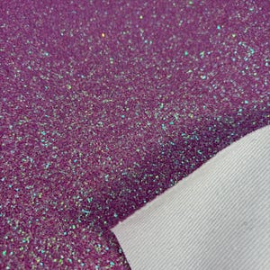 May include: Close-up of a sheet of purple glitter fabric. The fabric is covered in small, sparkling glitter particles that catch the light. The underside of the fabric is a plain white material.