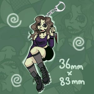 Könnte beinhalten: Ein Cartoon-Schlüsselanhänger mit einer sitzenden Figur mit braunen Haaren, die ein lila Oberteil, schwarze Shorts und Stiefel trägt. Die Figur hält ein blutiges Messer. Der Schlüsselanhänger ist 3,6 cm x 8,3 cm groß.