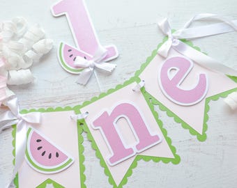 Puede incluir: Una guirnalda rosa y verde con temática de sandía con la palabra "one". La guirnalda incluye el número "1" y recortes de rodajas de sandía. Cintas y lazos blancos están unidos a las piezas de la guirnalda. Perfecto para una fiesta de primer cumpleaños.