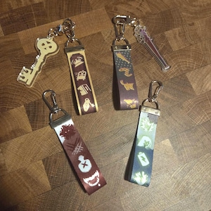 Può includere: Quattro portachiavi con vari disegni. Un portachiavi ha un ciondolo trasparente a forma di chiave. Gli altri portachiavi hanno cinturini in tessuto fantasia con chiusure in metallo color argento. I cinturini presentano diverse icone in bianco e oro.