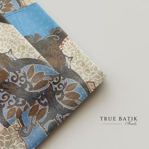 May include: Folded fabric with a batik pattern in shades of blue, brown, and cream. The design features stylized floral and geometric shapes. The text "TRUE BATIK Finds" is visible in the lower right corner.