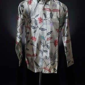 Peut inclure: Chemise à manches longues avec un motif floral rouge, gris et bleu sur fond clair. La chemise est présentée sur un mannequin noir sur fond noir. La chemise a une poche sur le côté gauche.