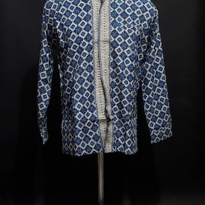 Może przedstawiać: Koszula zapinana na guziki z długim rękawem z niebiesko-białym geometrycznym wzorem. Koszula ma kontrastujący beżowy panel z przodu i jest prezentowana na manekinie. Koszula jest wykonana z lekkiej tkaniny.