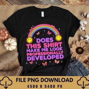 Peut inclure: Un t-shirt noir à manches courtes orné d'un arc-en-ciel coloré, de deux soleils souriants et de papillons. Le texte indique : DOES THIS SHIRT MAKE ME LOOK PROFESSIONALLY DEVELOPED. Le motif inclut de petites étoiles blanches dispersées.