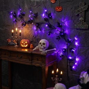 Könnte beinhalten: Eine Halloween-Dekoration mit einem geschnitzten Kürbis, einem Totenkopf und einer Skeletthand auf einem Holztisch. Lila Lichterketten und dekorative Zweige schmücken die dunkle Steinmauer. Ein dekoratives Kreuz und Kürbisdekorationen vervollständigen die Szene.