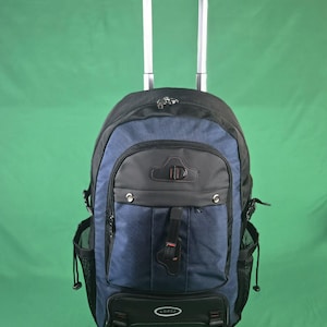 May include: A navy blue and black rolling backpack with a telescoping handle. The backpack has multiple compartments, including side mesh pockets and a front pocket with the brand name "LORCA". The handle is silver.