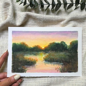 Op de afbeelding: Een rechthoekig landschapsschilderij op papier met een zonsondergang boven een kalme rivier. De lucht verloopt van zachte paarse naar gele tinten boven donkergroene bomen. Het water reflecteert het warme licht, omringd door weelderige oevervegetatie.