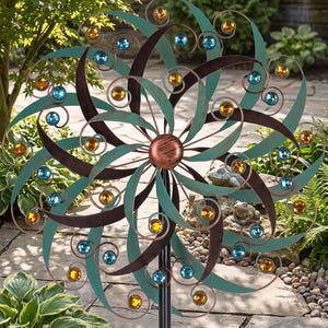 May include: A metal wind spinner featuring a circular design with curved teal and dark brown blades. The structure is accented with numerous round, faceted amber and blue glass gems placed at the ends of the spiraling metal wire arms.