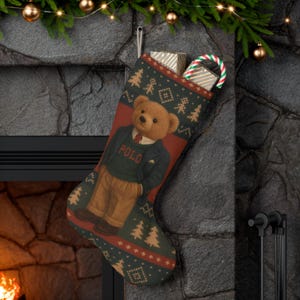 Könnte beinhalten: Weihnachtsstrumpf mit einem Teddybär, der einen Pullover mit der Aufschrift "POLO" trägt. Der grüne Strumpf hat einen roten Streifen und ein Muster aus Bäumen und Sternen. Er ist mit Geschenken und einer Zuckerstange gefüllt.