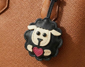 May include: A close-up of a brown leather handbag with a black and white sheep-shaped charm. The charm has a pink heart and is attached to a black leather strap. The handbag has a textured surface.
