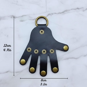 May include: A black leather hand-shaped keychain with brass-colored rivets and a ring. The keychain measures 4.7 inches (12 cm) in height and 3.1 inches (8 cm) in width.