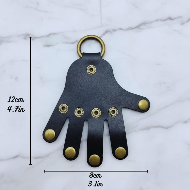 May include: A black leather hand-shaped keychain with brass-colored rivets and a ring. The keychain measures 4.7 inches (12 cm) in height and 3.1 inches (8 cm) in width.