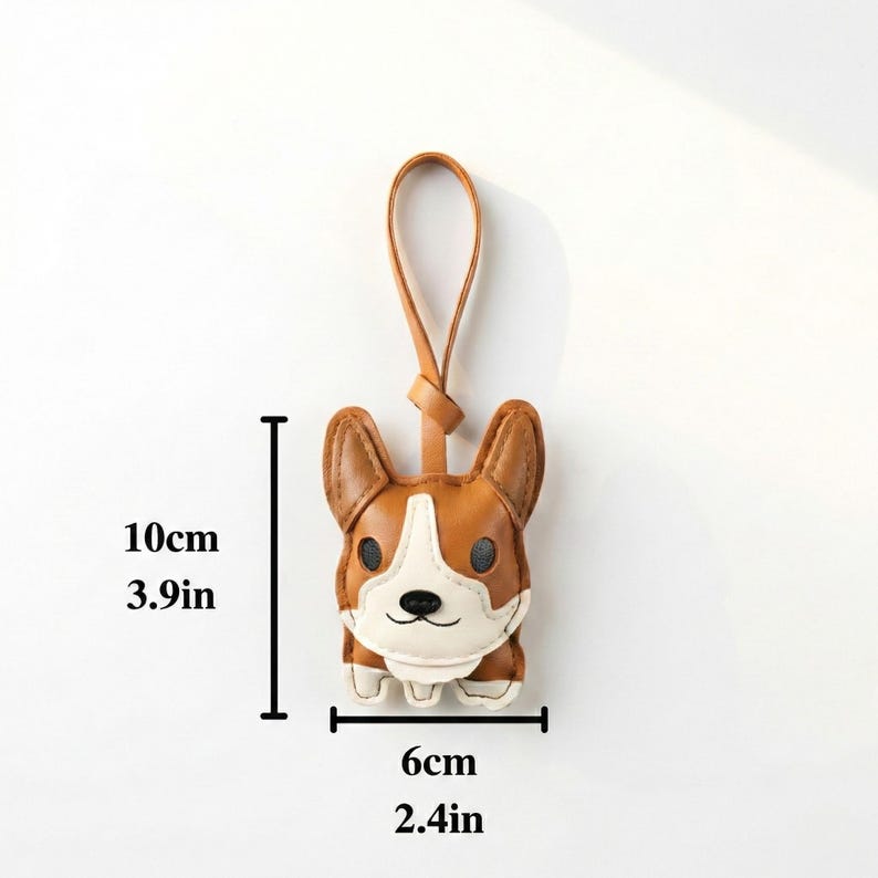 May include: A brown and white corgi-shaped keychain, 3.9 inches tall and 2.4 inches wide, with a leather loop. The keychain features a detailed design of a corgi's face and body.