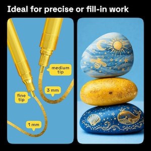 May include: Two gold metallic markers with fine and medium tips, creating 1 mm and 3 mm lines, respectively. The image also shows three painted stones in blue, yellow, and blue, with celestial and marine designs. The text reads "Ideal for precise or fill-in work."