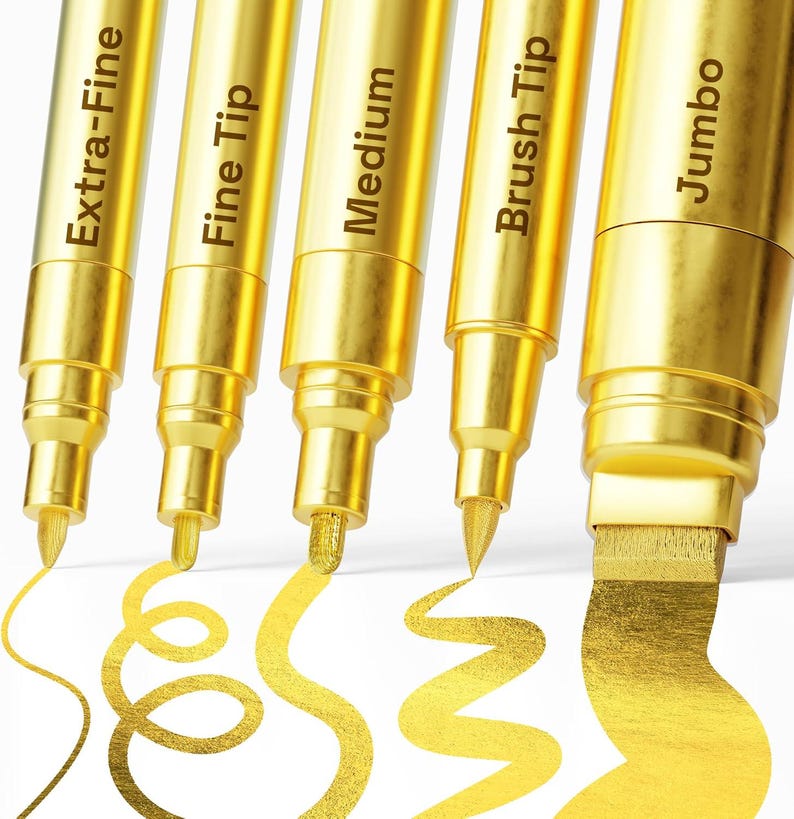 May include: Close-up of five gold metallic markers with different tip sizes: Extra-Fine, Fine Tip, Medium, Brush Tip, and Jumbo. Each marker is labeled with its tip type. Gold ink strokes are visible, showcasing the different line widths.