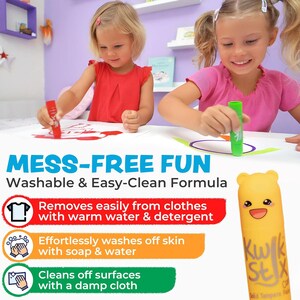 May include: Two young children are shown using washable, easy-clean formula art sticks. The image highlights the product's features: removes easily from clothes, washes off skin with soap and water, and cleans off surfaces with a damp cloth. The text reads "MESS-FREE FUN".