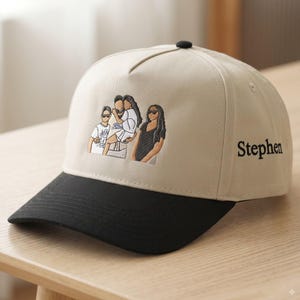 May include: A beige baseball cap with a black brim and a black button on top. The front features an embroidered graphic of three people, and the side is embroidered with the name Stephen in black lettering. The cap has a structured five-panel design.