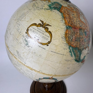 May include: A vintage Replogle World Classic globe, 9-inch diameter, mounted on a dark wooden base. The globe features detailed cartography with a cream-colored surface and colorful continents. The globe has a brass-colored meridian and a decorative label.