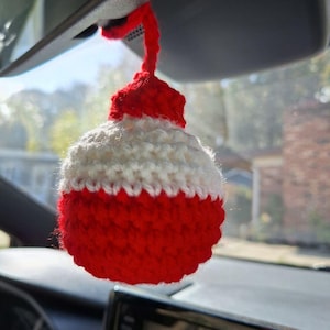 May include: A red and white crocheted bobble hanging from a car's rearview mirror.
