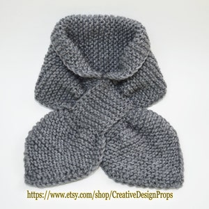 May include: Gray knitted scarf with a wide collar. The scarf is folded in half and the ends are tied together.