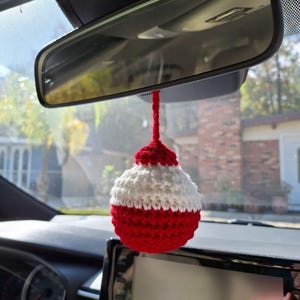 May include: A red and white crocheted fishing bobber hanging from a rearview mirror in a car.