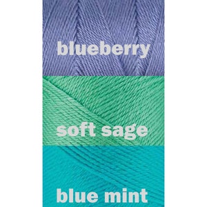 May include: Three skeins of yarn in different shades of blue and green. The top skein is a light blue color labeled "blueberry". The middle skein is a light green color labeled "soft sage". The bottom skein is a turquoise color labeled "blue mint".