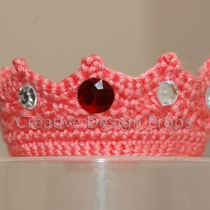 May include: A pink crocheted crown with a red jewel and clear rhinestones.