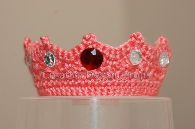 May include: A pink crocheted crown with a red jewel and clear rhinestones.