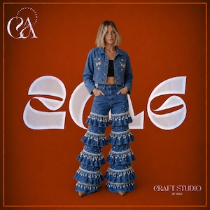 May include: A blue denim jacket with white floral embroidery on the chest and matching blue denim flared trousers featuring four tiers of ruffled hems adorned with white pearl-like beads. The outfit is worn over a simple black crop top.