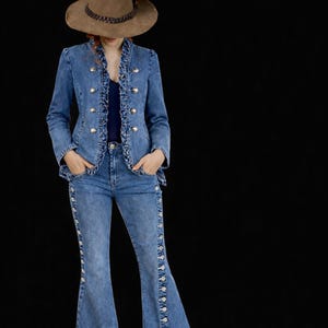 May include: A denim jacket and flared jeans ensemble. The jacket features gold buttons and ruffled trim. The jeans have decorative buttons down the sides. A brown hat with a beaded band completes the outfit. The text "CRAFTSTUDIOBYMALIK" is at the top.