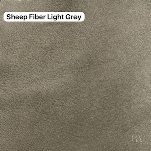 May include: A close-up of a light grey sheep fiber fabric. The fabric has a textured surface and the words "Sheep Fiber Light Grey" are displayed in a white rectangular box in the upper left corner.